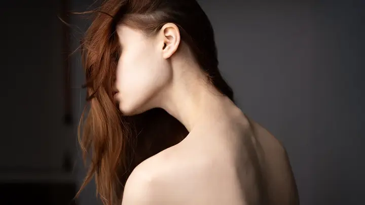 A woman with beautiful healthy hair falling over her face showing the slender and pale back of her neck