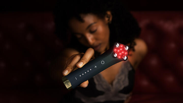 A blurry woman in the shadows holding FAQ 402 dual microcurrent and NIR facial toning device in a closeup main frame