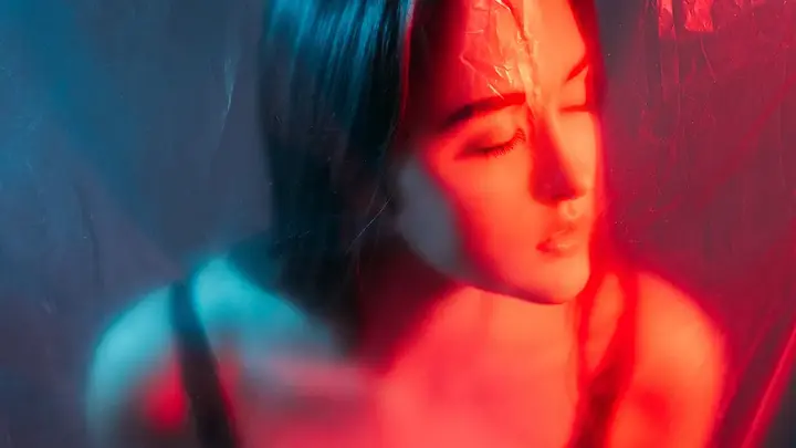 A woman behind a translucent barrier, eyes closed and illuminated by red light therapy