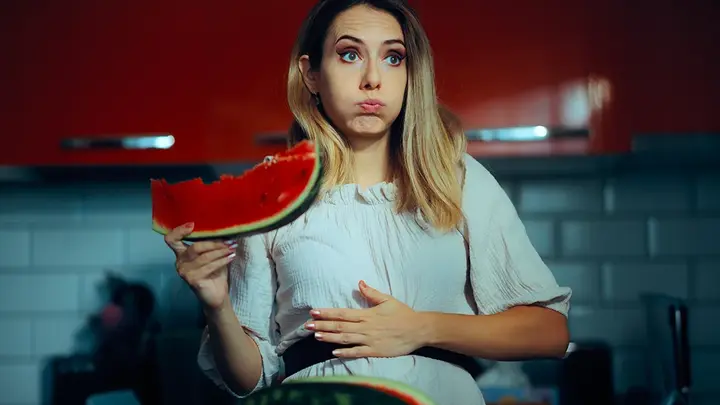A bloated woman eating a watermellon  