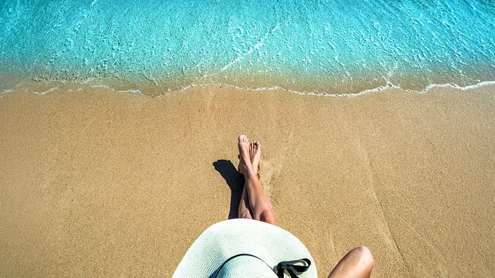 A woman in a white wide-brimmed hat sitting on a beautiful sandy beach