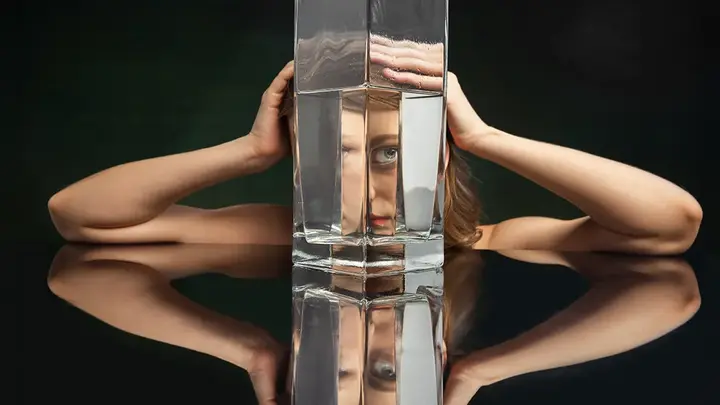 A woman on a black backgorund looking through a huge jug of water defoirming her features