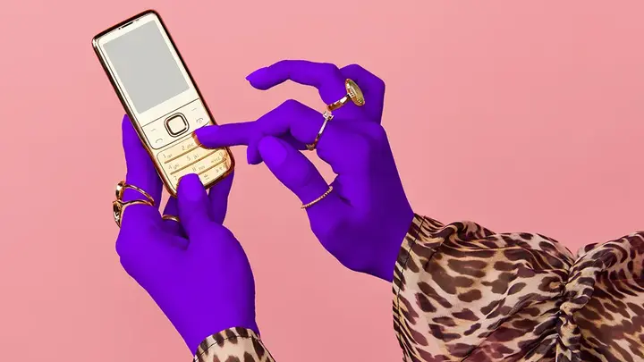 Hands of a woman in a lepard print shirt and with purple gloves, scrolling on a phone