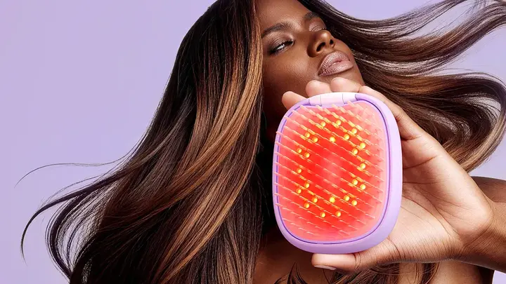 An African-American woman using a red light brush and flipping her fabulous, lush, smooth hair on a pink background