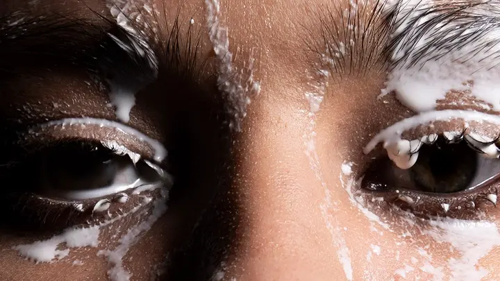 A closeup uf a womans eyes and a cleansing product dripping over her face