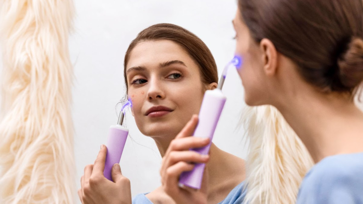 Female model reflected in the mirror treating her face with FOREO ESPADA 2 plus acne treatment device