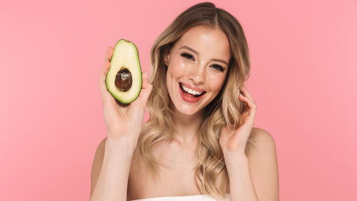 Vitaminas y cuidado facial. Una mujer sostiene un aguacate.