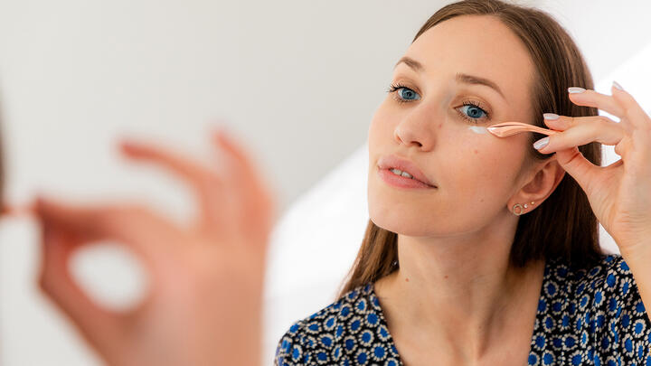 Young woman reflected in a mirror applying serum under her eyes